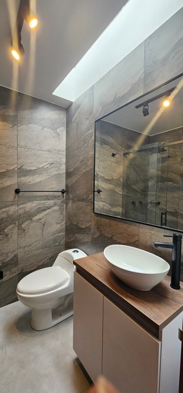 Este proyecto consistió en el rediseño completo de un baño, optimizando la distribución, la funcionalidad y la estética del espacio. Se emplearon materiales de alta calidad como porcelanatos de gran formato con acabado tipo piedra, mobiliario a medida con cubierta de madera y accesorios en negro mate. La iluminación puntual y la entrada de luz natural a través de un domo superior generan una atmósfera cálida y sofisticada.<br />
<a href="/cajica" class="btn-proyecto" target="_blank">Ver Proyecto</a> Remodelación integral de baño